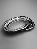 Set of two polished stainless steel oval trays with scalloped edges and smooth surfaces.