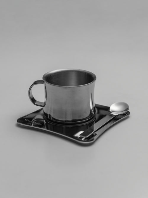 Stainless steel coffee cup with handle on black square tray with a small spoon.