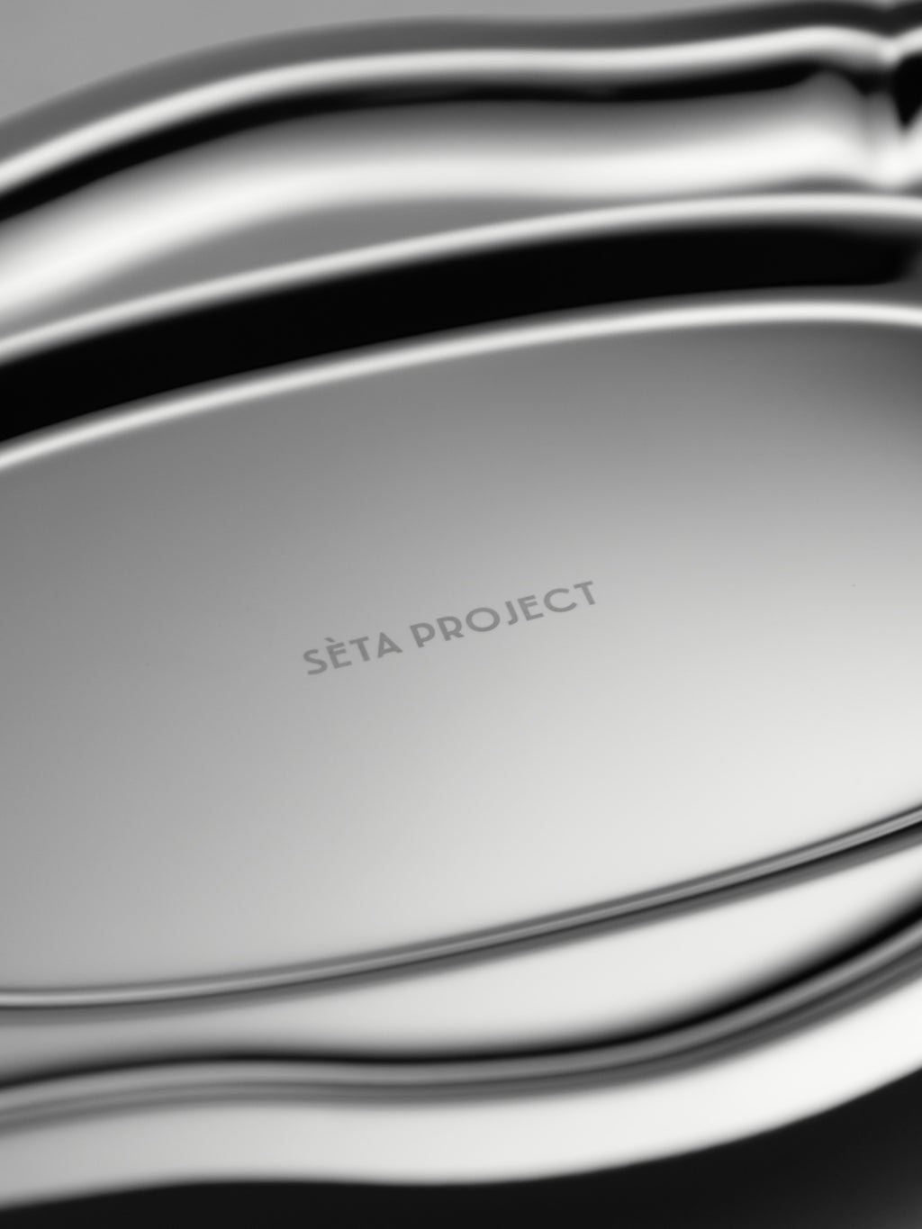 Oval stainless steel tray with smooth, curved edges and polished finish, engraved "SETA PROJECT" at the center.