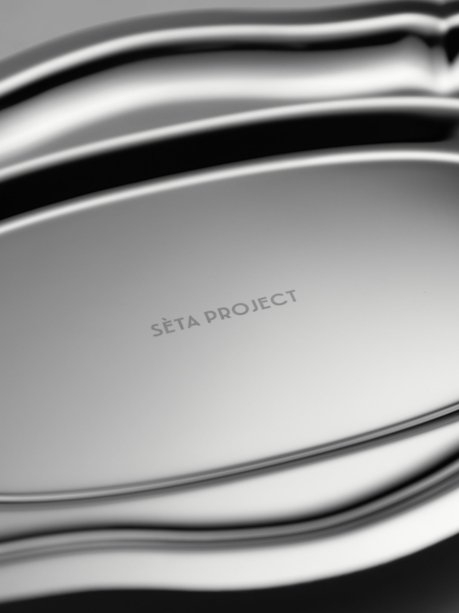 Oval stainless steel tray with smooth, curved edges and polished finish, engraved "SETA PROJECT" at the center.