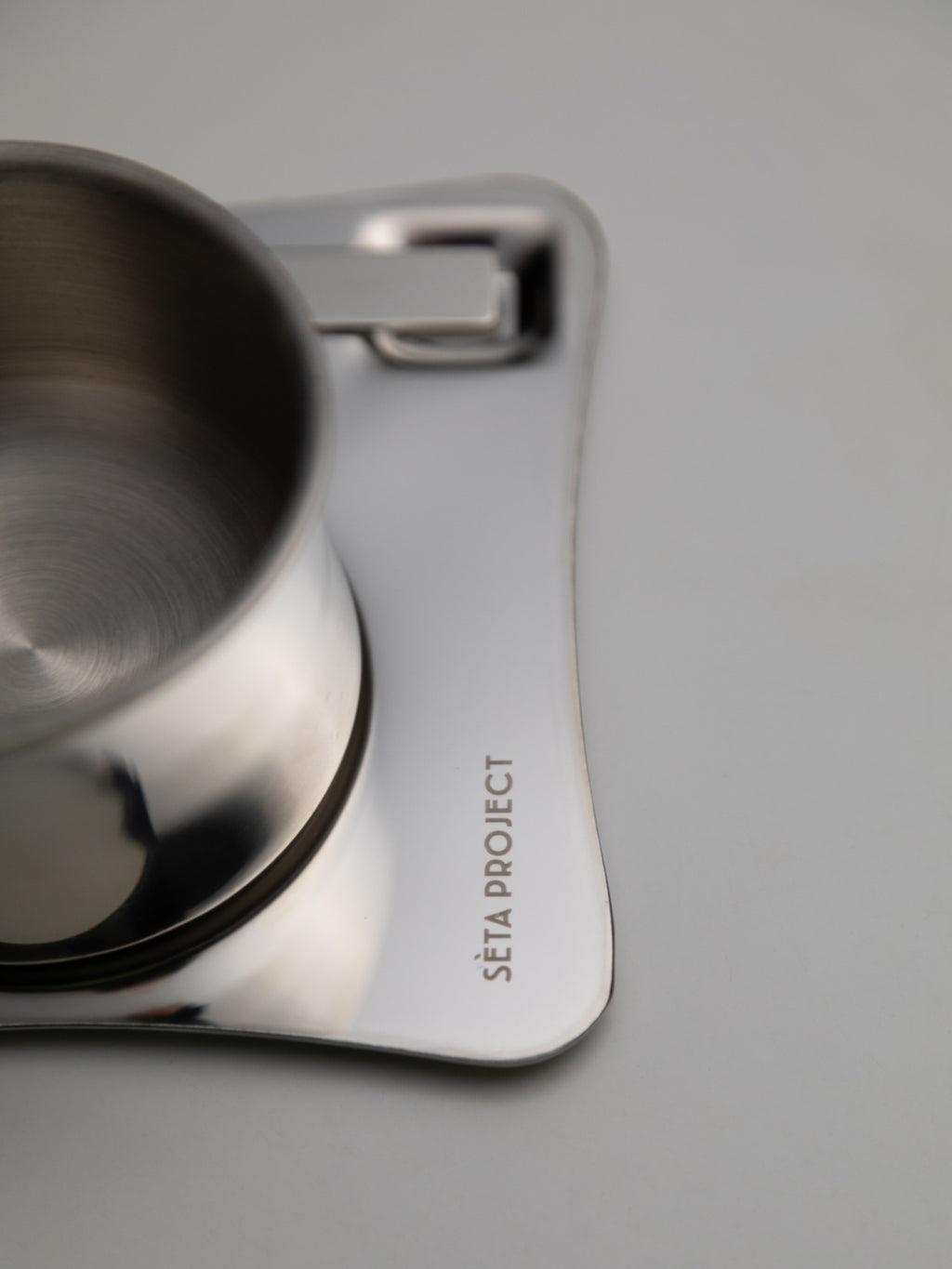 Stainless steel CHROMA ARC coffee cup with curved square saucer engraved with brand name.