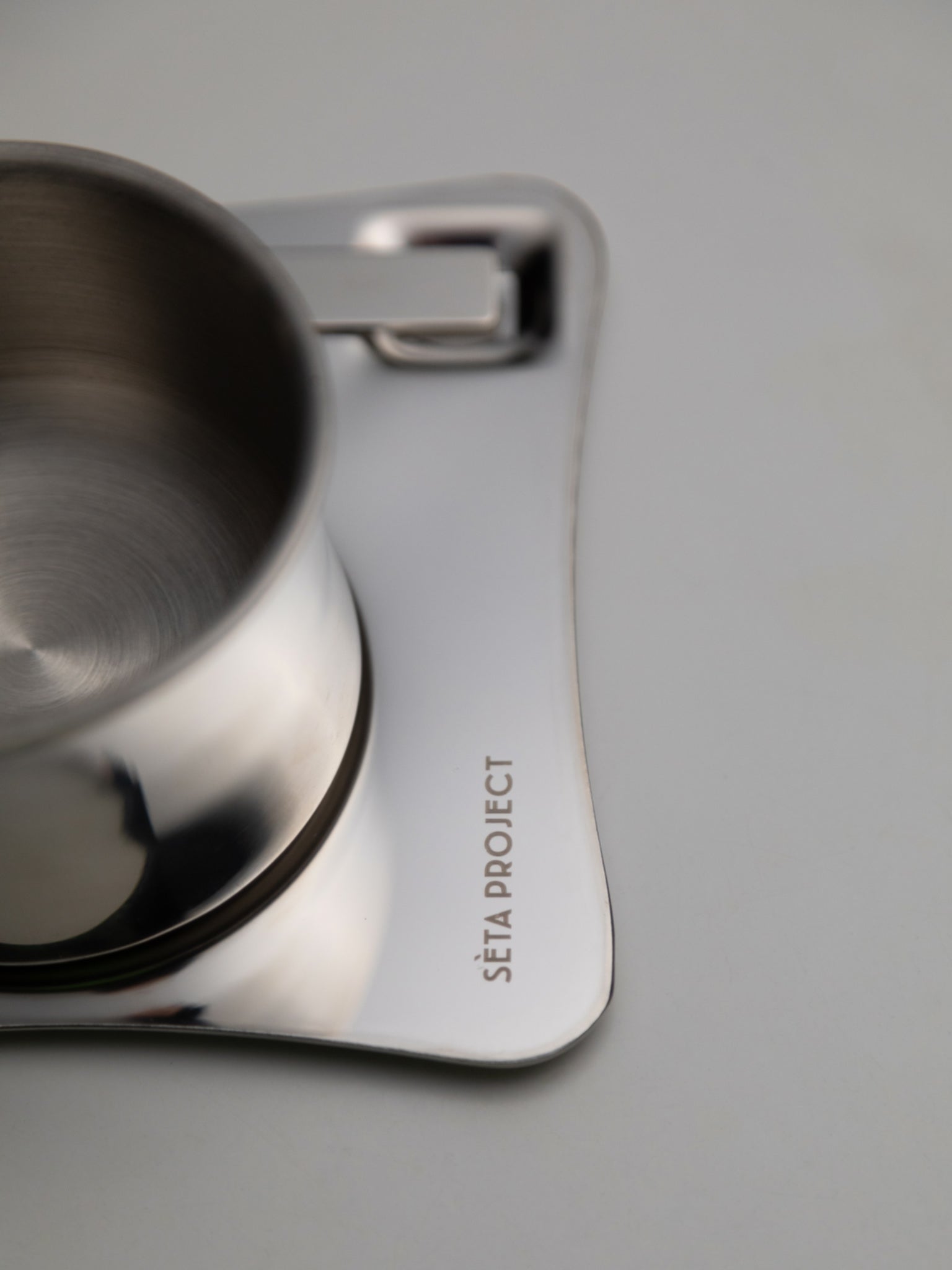 Stainless steel CHROMA ARC coffee cup with curved square saucer engraved with brand name.