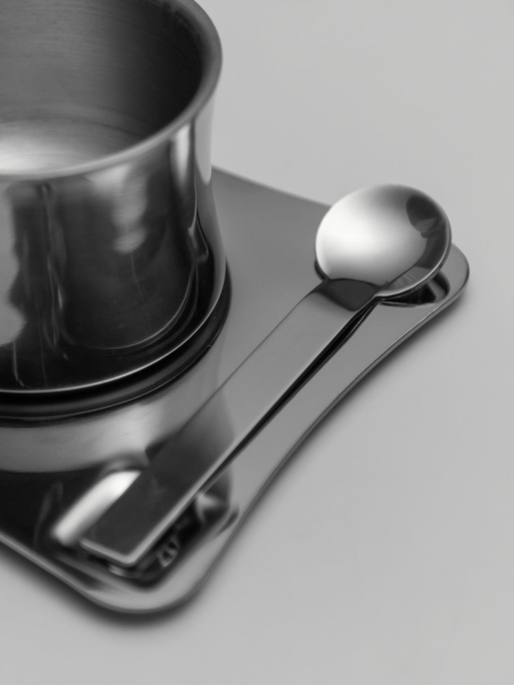 Stainless steel coffee cup with matching spoon resting on a sleek metal tray.