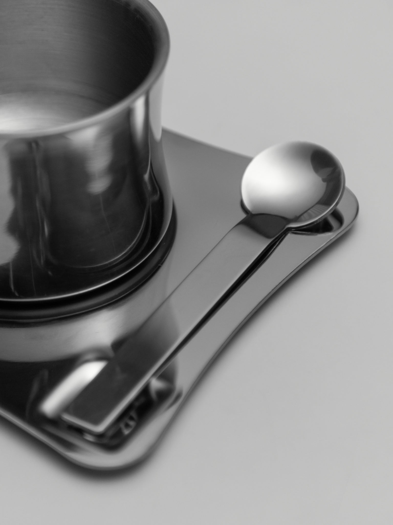 Stainless steel coffee cup with matching spoon resting on a sleek metal tray.