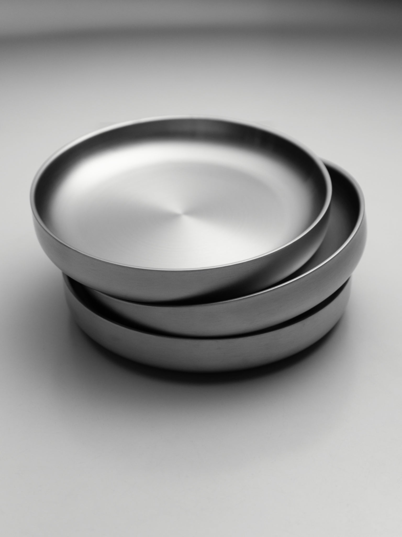 Stack of three round stainless steel plates with flat edges and brushed finish on gray background.