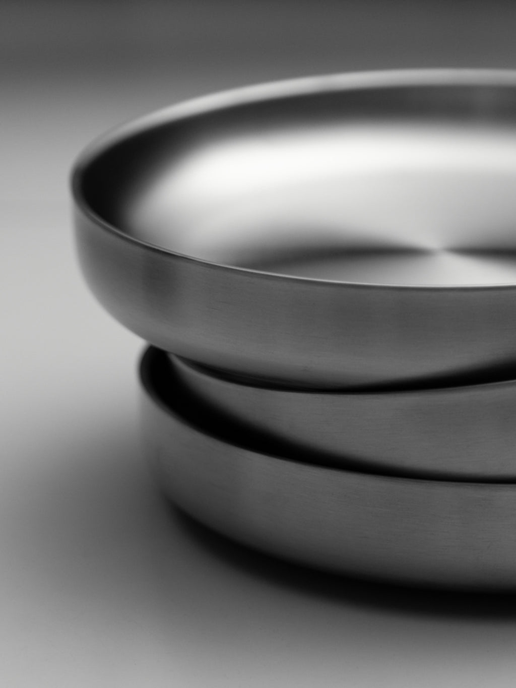 Stacked round stainless steel plates with smooth, polished rims on a white surface.