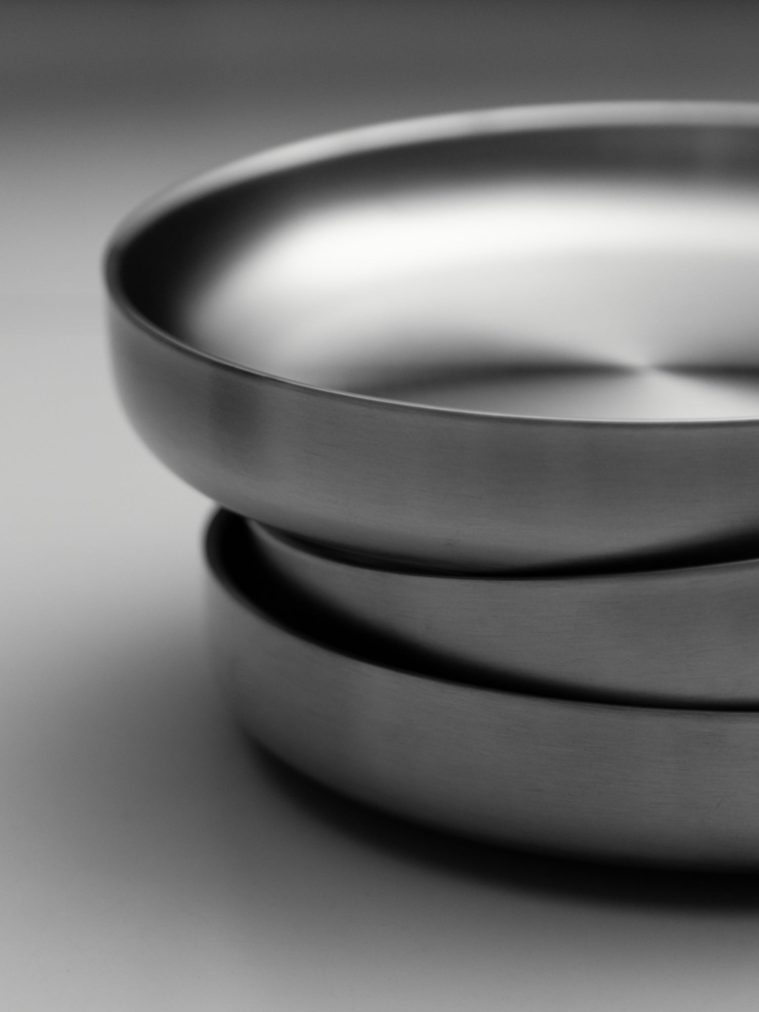 Stacked round stainless steel plates with smooth, polished rims on a white surface.