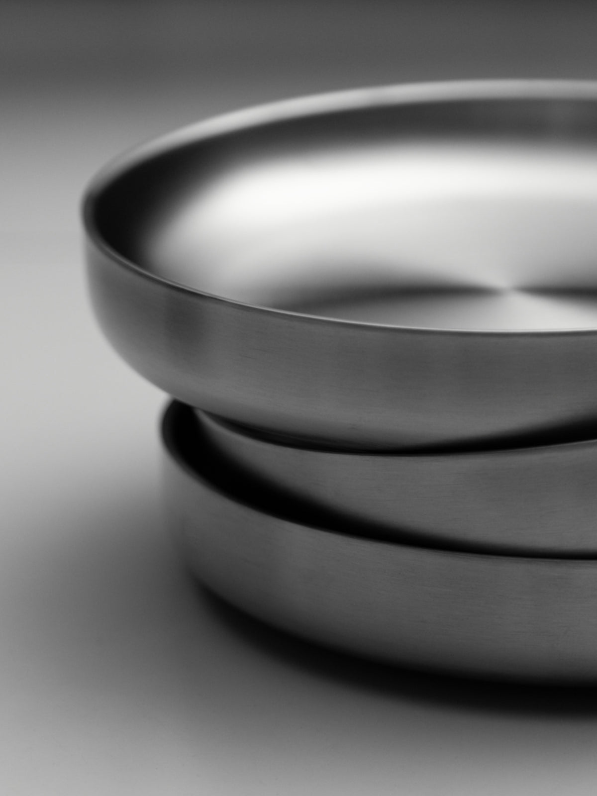 Stacked round stainless steel plates with smooth, polished rims on a white surface.